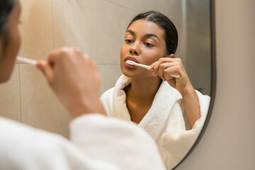 Woman wearing white bathrobe brushing her teeth