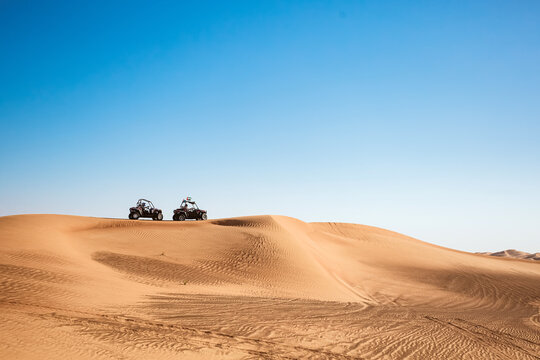 Silhouettes of two buggy quad bikes up on sand hill at blue sky background, safari tour motor vehicles for extreme sports
