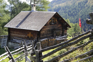 Altesholzhaus mit der Schweizfahne in den Bergen. Vorne Holzzaun, Hinten Bergen, Bäume, Landschaft