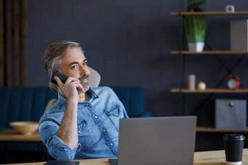 Senior grey-haired businessman talking on the phone in office. Conversation with business partners. Business portrait of handsome mature man sitting at workplace. Communication, negotiation.