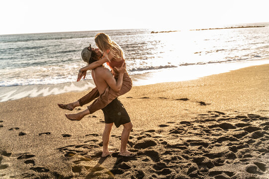 Beautiful couple of young multiethnic people kissing on the beach, having fun together. Real people emotions. Summer surfers lifestyle concept.