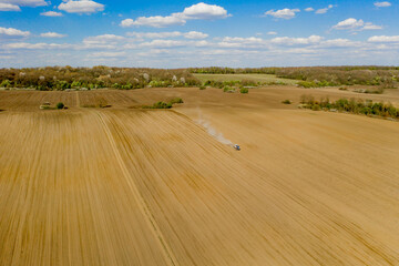 Obraz premium Aerial view large tractor cultivating a dry field. Top down aerial view tractor cultivating ground and seeding a dry field. Aerial tractor cuts furrows in farm field for sowing