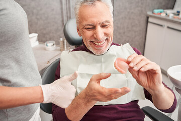Dentist showing to senior patient teeth dentures - 415487135