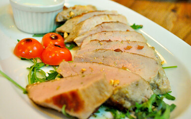Juicy pork with green salad and cherry tomatoes on white plate. Restaurant meal. Creative way of cooking.