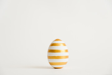 Easter golden with striped patternd egg isolated on white background. Minimal easter concept. Happy Easter card with copy space for text. Top view, flatlay. Concept for banner, flyer, invitation