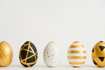 Easter golden decorated eggs stand in a row on white background. Minimal easter concept. Happy Easter card with copy space for text. Top view, flatlay.