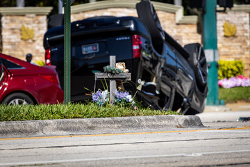 SUV flipped over on its roof with a cross remembering another victim on the traffic median.