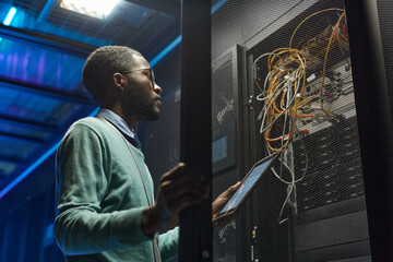 Low angle portrait of African American data engineer holding digital tablet while working with...