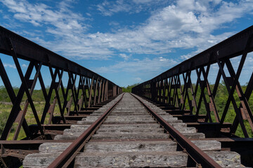 Fototapeta na wymiar Abandoned iron railway bridge over a stream with a sky and clouds background