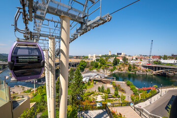 A gondola with tourists flies over Riverfront Park and the Spokane Falls Dam near the Water and Power building in downtown Spokane, Washington USA at summer.