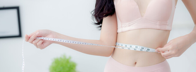 Beautiful young asian woman sexy body slim measuring abdomen for control weight loss in the room,...
