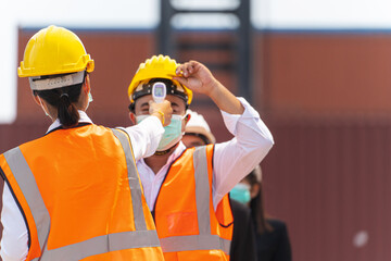 Factory woman worker in a face medical mask and safety dress used measures temperature at worker...