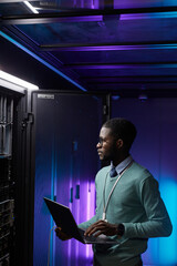 Vertical portrait of young African American data engineer holding laptop while working with...