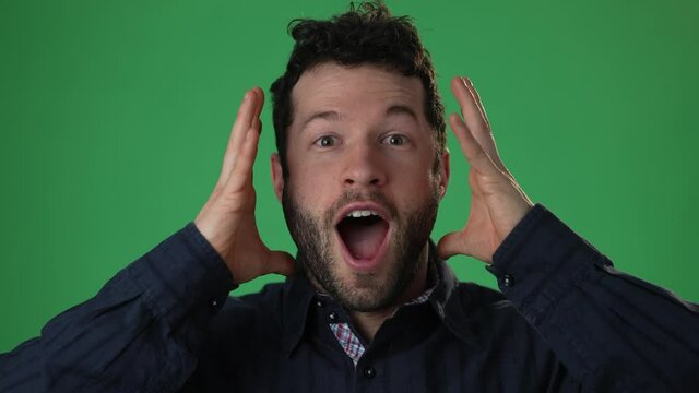 Closeup slow motion portrait of amazed man shocked, saying WOW. Handsome hip guy with stylish hairdo surprised to camera on green screen chroma key background.