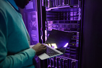 Cropped shot of African American data engineer holding laptop while working with supercomputer in...