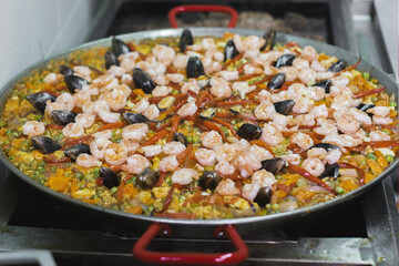 Una paella con pulpo, carne, camarones, mejillones, pimentón rojo, habichuelas, alverjas y zanahoria dentro de una olla en el fogón de una cocina