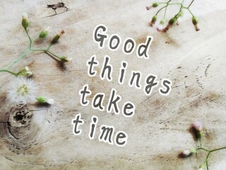 Good things take time, text on wood board background with grass flowers