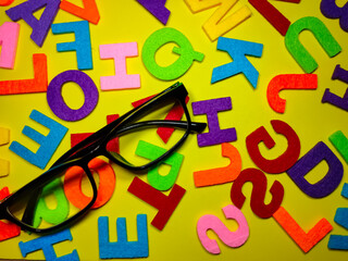 Selective focus.Eye glasses and colorful word on yellow background.Education concept.Shot were noise and film grain.