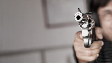 Woman pointing a gun at the target. Close-up image of the muzzle of a gun on dark background,...