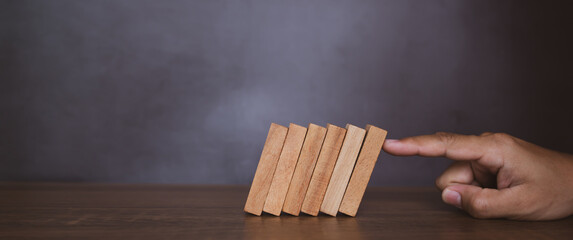 Close-up fingers prevent the wooden block from falling domino concepts of financial risk management and strategic planning.