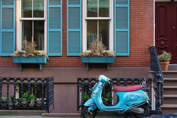 Retro looking blue scooter parked on a sidewalk in front of a brownstone