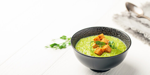 Green peas soup with breadcrumbs in a bowl on a white wooden table. Copy space