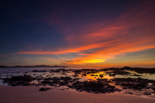 Tropical summer sunset landscape at the beach with sand, rocks, water, calm ocean, colorful blue sky with orange clouds, Flamingo Beach, Guanacaste, Costa Rica