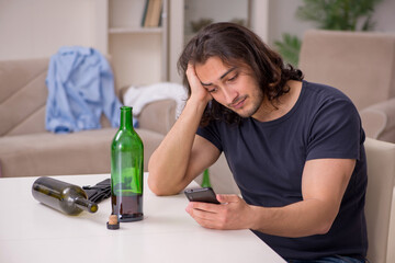 Young unemployed man drinking alcohol at home