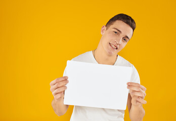 A man in a white T-shirt with a sheet of paper on a yellow background Copy Space mockup