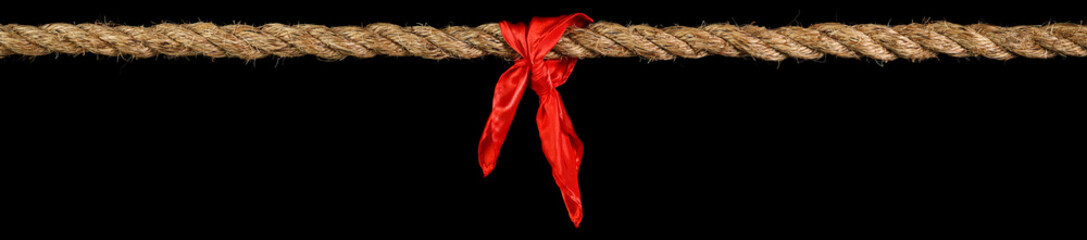 Long tug of war rope pulled tight, with red ribbon tie. Concept of conflict, competition, or rivalry. Isolated on black.