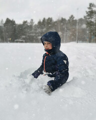 Fototapeta na wymiar happy child in winter clothes sitting in a snowdrift