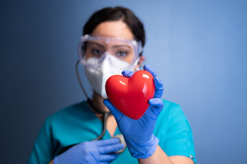 young female healthcare worker in mask and goggles, holding a heart