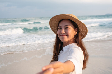 A beautiful young asian woman holding hand and leading her boyfriend to the beach for follow me concept