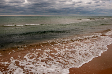 Fototapeta premium Black Sea. Water with waves. Dark cloudy weather. Deep bright blue water. Before storm. Sand coast 