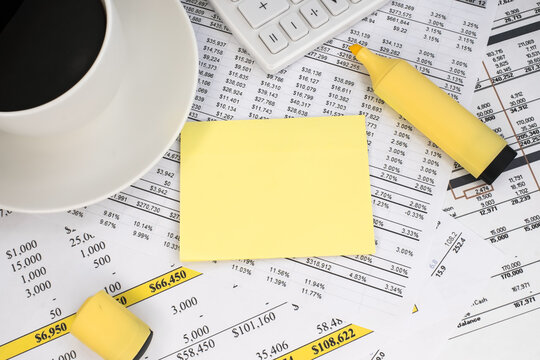 A yellow blank sheet with a yellow marker and a white coffee cup on the financial documents. Business and financial concept