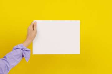 Empty space for text. A white sheet of paper in a hand. Yellow background.