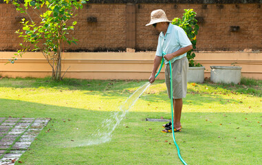 senior asian reitred man using hose to watering lawn in backyard in morning