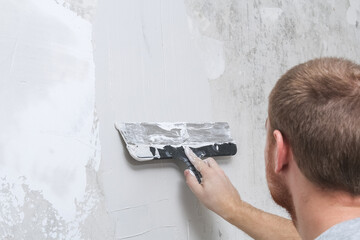 A male worker spreads the putty mixture and flattens the wall.