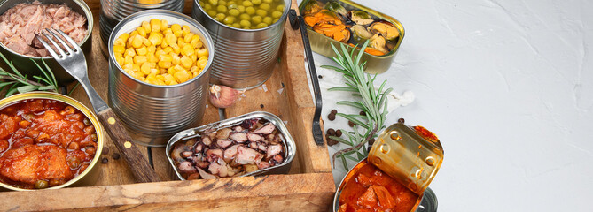 Various canned vegetables, fish and peas in aluminum cans on light gray background.