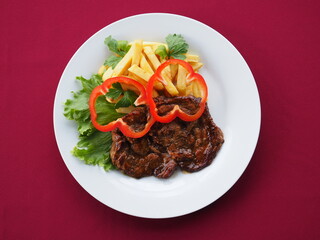 Beefsteak with tomato and herbs on a red background