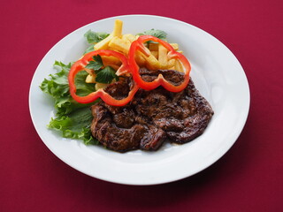 Beefsteak with tomato and herbs on a red background
