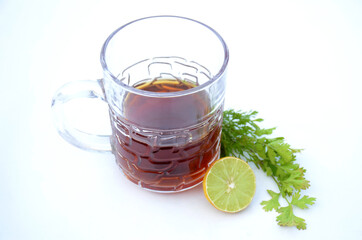 the black lemon tea in the glass cup with anise and lemon on the white background.