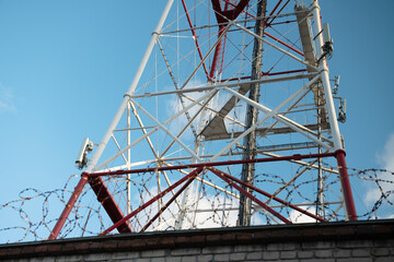 Telecommunication tower against the blue sky, with barbed wire. TV tower. Forbidden zone