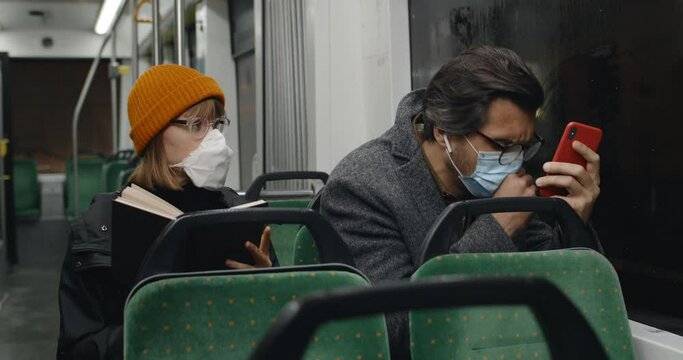 Woman with book stand up and go away when guy sitting next to her in tram started coughing. People in medical masks commuting in public transport. Concept of pandemic, illness, quarantine.