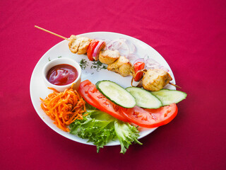 Chicken kebab with tomato and greens on a red background