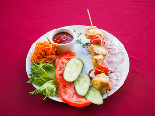 Chicken kebab with tomato and greens on a red background