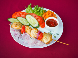 Chicken kebab with tomato and greens on a red background
