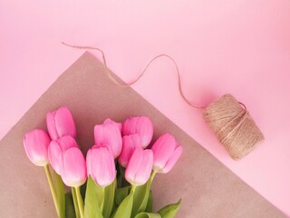Obraz na płótnie Canvas Pink tulips in craft paper on pink background. Florist preparing bouquet of fresh beautiful tulips. Easter, Valentine's Day, Mother's day. Spring card. Place for text. Minimalism