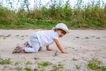 cute happy toddler in a cap crawls on all fours along a country road in the sand on a sunny summer day