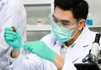 Male researcher wearing hyhiene protective mask and safety eyeglases dropping liquid into test tube